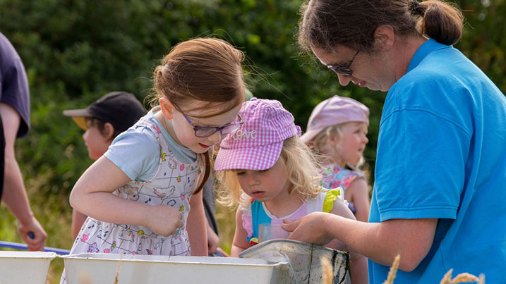 Children and WWT staff peering into a pond dipping bowl
