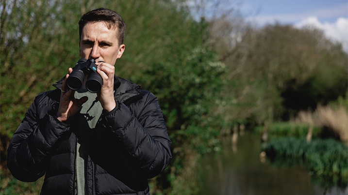 A man uses binoculars against a wetland background