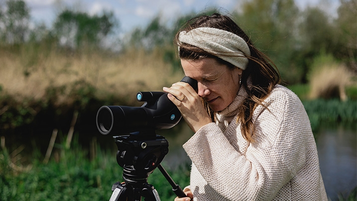 A lady uses a telescope against a wetland background