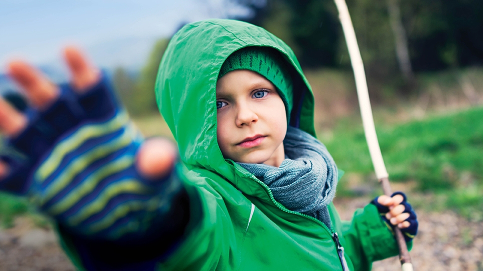 Child reaching out their hand to the camera while holding a willow wand.